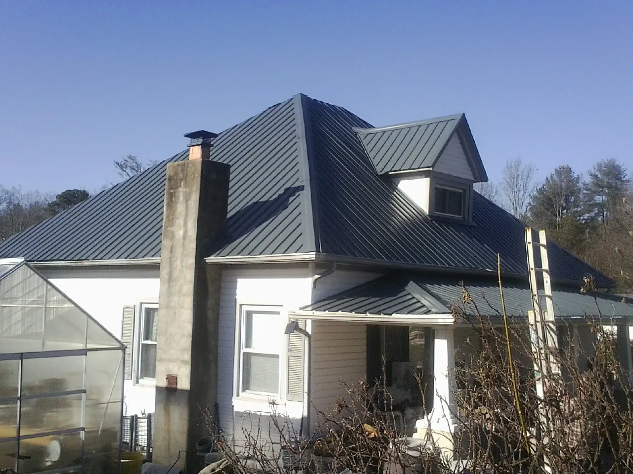 Dark blue standing seam metal roof on a white farmhouse with dormer — Slate & Tile Roof Repair by Roofing Brothers in Harmans