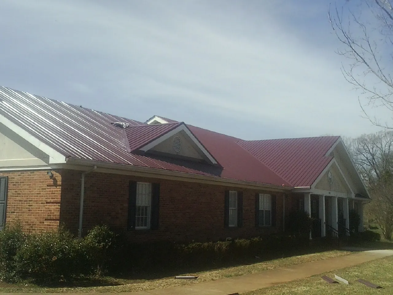 Red metal roof with gabled entries on a long brick building, from a Hail Damage Roof Repair job in Harmans