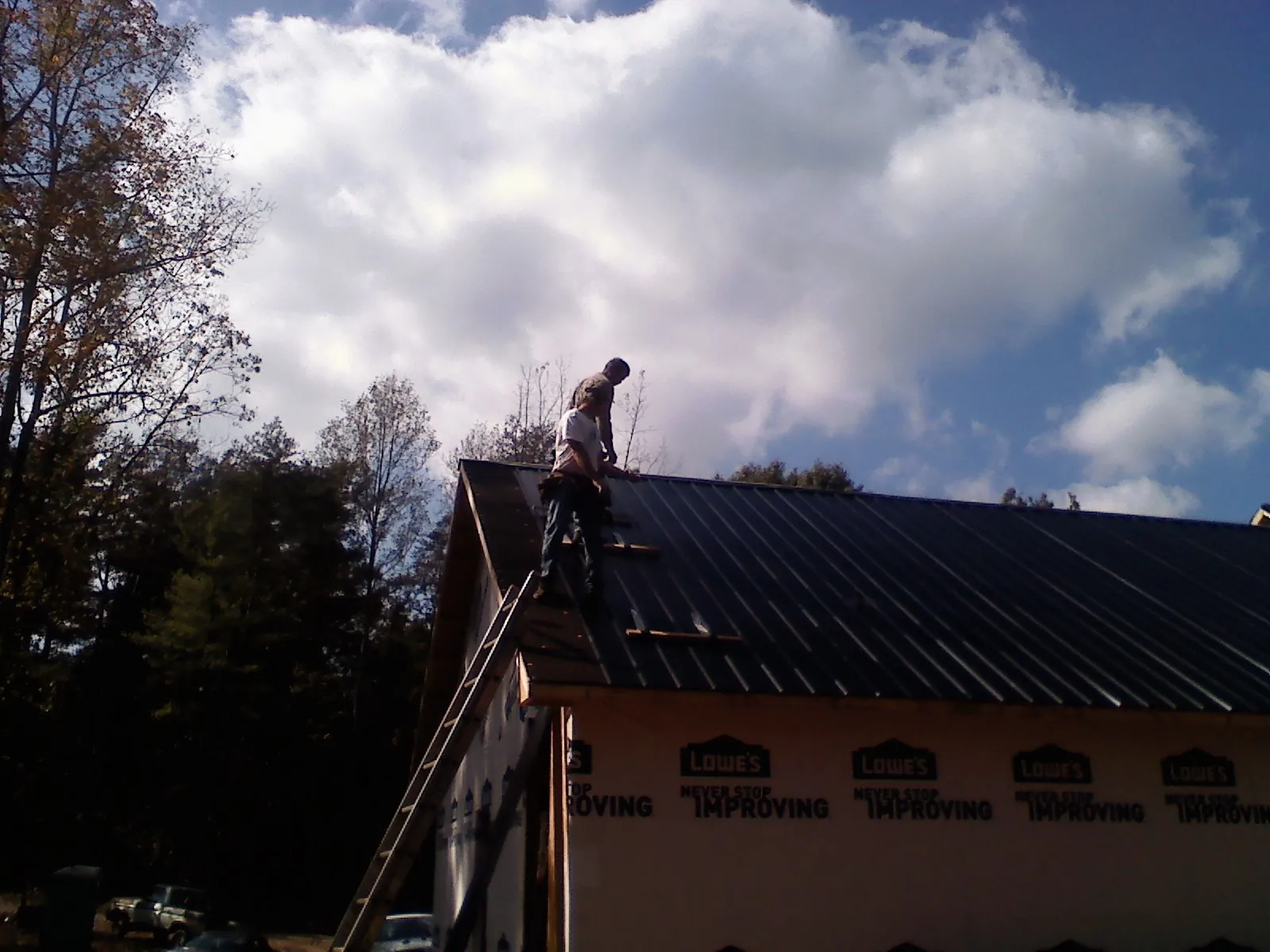 Roofer fastening dark metal panels high against a cloudy sky, from a Roof Inspection job in Harmans