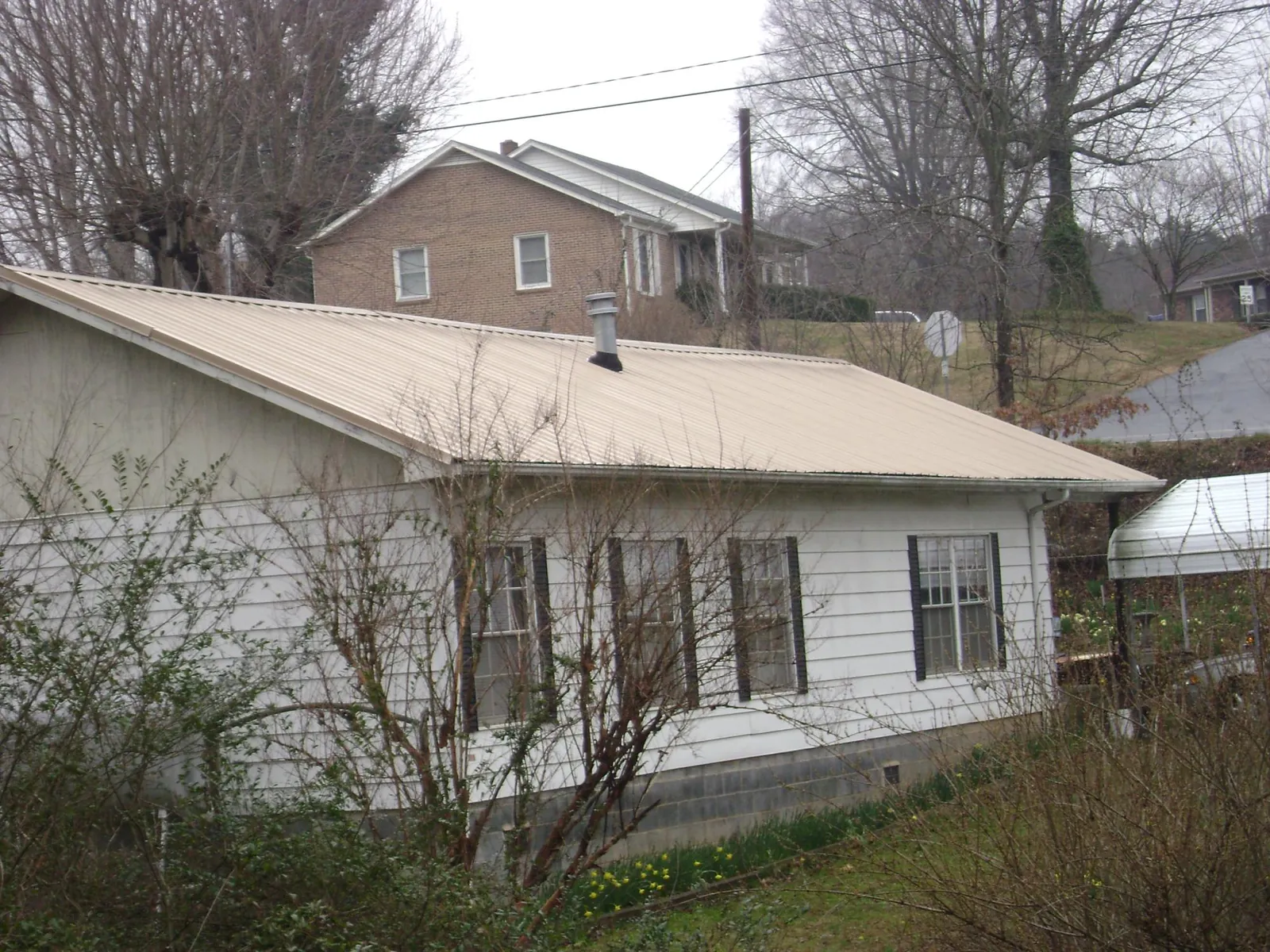 Tan metal roof on a white sided house set into a hillside — Commercial Roofing by Roofing Brothers in Harmans